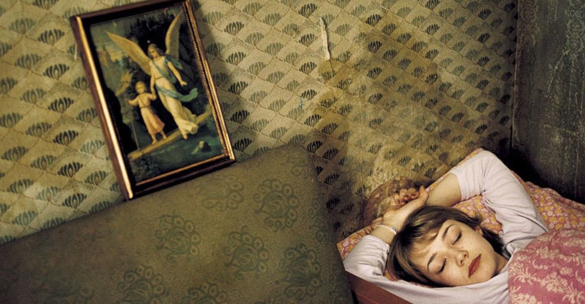 A girl sleeps under a floral blanket in a room with patterned wallpaper.