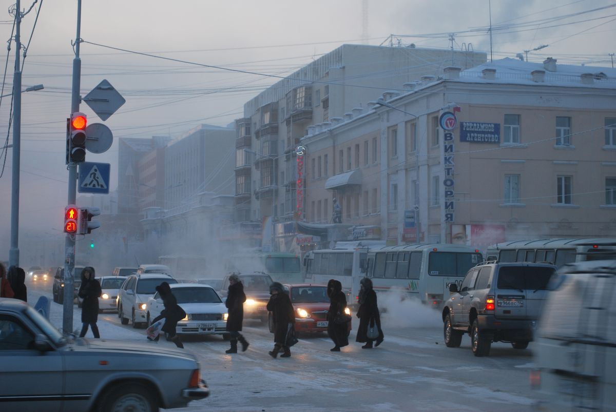 Pedestrians cross a snowy street in Yakutsk as cars and buses pass through the winter mist.